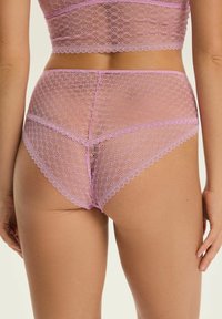 Różowe koronkowe majtki z wysokim stanem i pasujący crop top noszone przez stojącą osobę, ukazana od tyłu z rękami swobodnie opadającymi wzdłuż ciała.
