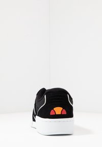 Baskets noires en matériaux mesh et suède, semelle en caoutchouc blanche, avec un logo coloré en orange et jaune au niveau du talon.