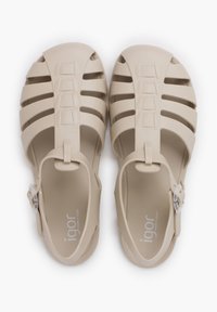 Sandalias de plástico beige con diseño de punta abierta, hebilla ajustable y lados ranurados para ventilación. Suela interior texturizada con logo.