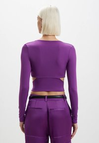 Maglietta viola a maniche lunghe con design a fessura in vita, realizzata in un tessuto liscio e elasticizzato. Presenta un colletto alto e una silhouette aderente.