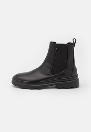 Stivale Chelsea in pelle nera con pannelli laterali elastici, linguetta per tirare, suola robusta e piccolo dettaglio in tessuto rosso-bianco-blu sul lato.
