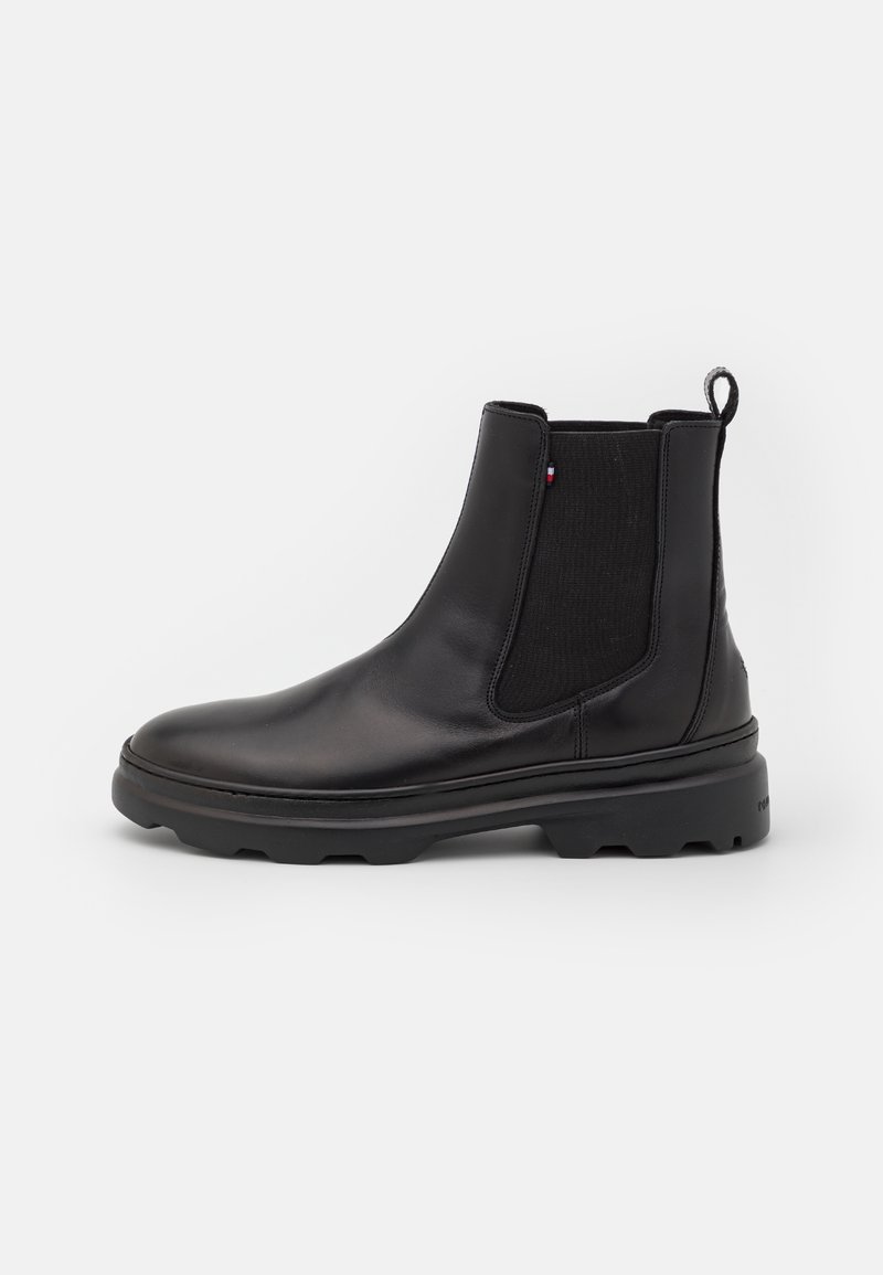 Botte Chelsea en cuir noir avec panneaux latéraux élastiques, languette de tirage, semelle robuste et petit détail en tissu rouge-blanc-bleu sur le côté.