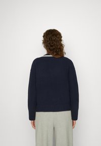 Granatowy sweter z dzianiny o żeberkowanej fakturze i szerokich rękawach. Posiada biały akcent na kołnierzu. W zestawie z jasnymi, luźnymi spodniami.