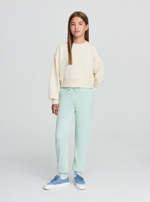 Kremowa krótka bluza z szerokimi rękawami i ściągaczem u dołu, zestawiona z jasnomiętowymi spodniami dresowymi z elastycznym pasem i sznurkiem do regulacji.