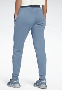 Ljust blå svettbyxor med en texturerad yta, som har sidofickor, elastisk midja och kontrasterande svarta och vita randiga detaljer.