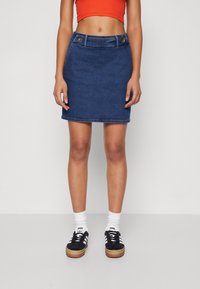 Jeanskjol i mörkblått, med en åtsittande silhuett, två framknappar och en fåll precis ovanför knäet. Kommer tillsammans med svarta sneakers.