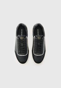 Sorte sneakers med glat syntetisk overdel, hvide accenter og sorte snørebånd. Har en blød indersål og gummisål med struktureret greb.