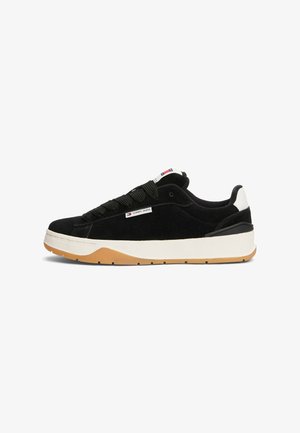 Black suede sneaker with white heel and sole, gum outsole, thick black laces, and "Tommy Jeans" logo tag on the side.