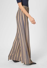 Wijde broek in een tan stof met verticale marineblauwe strepen, met een hoge taille en een gladde textuur. Draag het met zwarte puntige schoenen.