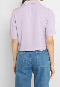 Lila, kortärmad, krage skjorta med en texturerad tyg; kort design. I kombination med högmidjade blå jeans med bakfickor.