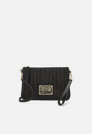 Bolso de mano de nailon negro acolchado con una placa de logo dorada y una correa desmontable. Presenta un diseño elegante y una superficie texturizada.