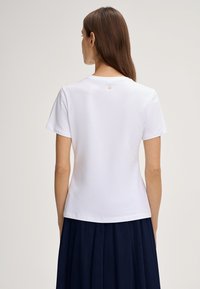 Wit T-shirt met korte mouwen en ronde hals, met een klein logo-accent op de achterkant. Zachte katoenen stof met een gladde textuur.