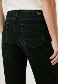 Mustad denimpüksid, millel on tagant vaadates kaks plaati taskut. Vööl on logo silt. Tekstuuriga kangas, millel on õrn värvikadu.