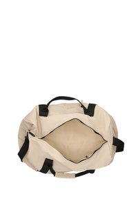 Bolsa de lona beige con correas y cremallera negras, que cuenta con un interior espacioso y una textura suave, adecuada para viajes o uso en el gimnasio.