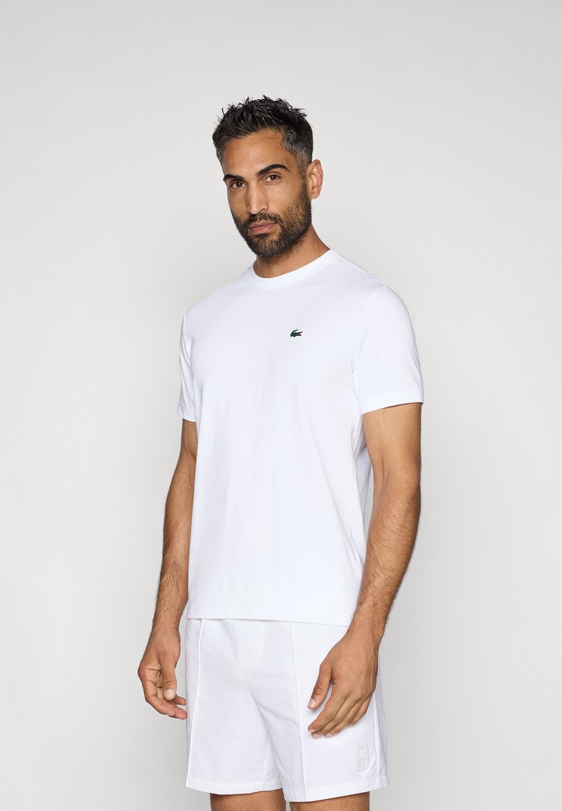 Λευκό μπλουζάκι με στρογγυλή λαιμόκοψη, φτιαγμένο από βαμβάκι, με ένα μικρό πράσινο λογότυπο στο αριστερό μέρος του στήθους. Κοντά μανίκια και άνετη εφαρμογή.