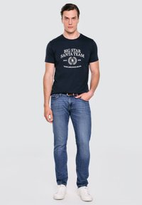 Námořnické tričko s bílým potiskem, spárované s světle modrými džíny a bílými teniskami. Jednoduchý volnočasový design s kulatým výstřihem.