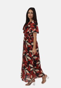 Maxikleid mit schwarzem Grund und großem roten und beigen Blumenmuster. Hat kurze Ärmel und einen elastischen Bund. Ergänzt durch transparente Sandalen mit Absatz.