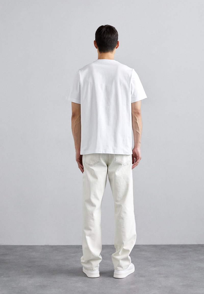 White cotton t-shirt with short sleeves, paired with light-colored jeans. The outfit is completed with white sneakers. Simple and minimal design.