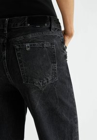 Jeans de mezclilla negra con un ajuste relajado, que incluyen un bolsillo trasero, un ligero desgaste y detalles en metal plateado.