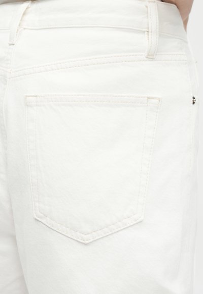 Κοντινό πλάνο λευκών τζιν denim που δείχνει την πίσω τσέπη και τη θηλιά της ζώνης στη δεξιά πλευρά του γοφού του ατόμου που τα φοράει.