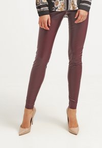 Bordowe legginsy z sztucznej skóry o gładkim, dopasowanym kroju. Noszone z cielistymi szpilkami, podkreślającymi błyszczącą fakturę.