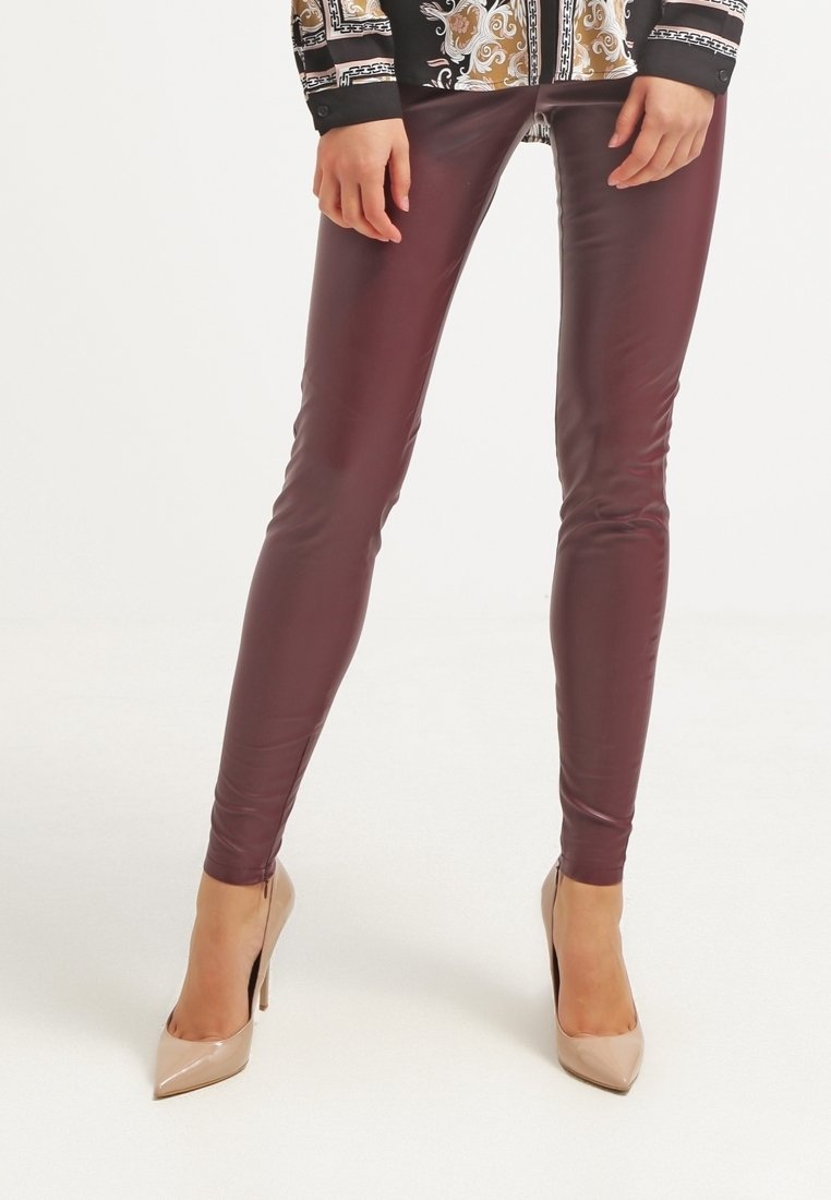 Bordowe legginsy z sztucznej skóry o gładkim, dopasowanym kroju. Noszone z cielistymi szpilkami, podkreślającymi błyszczącą fakturę.