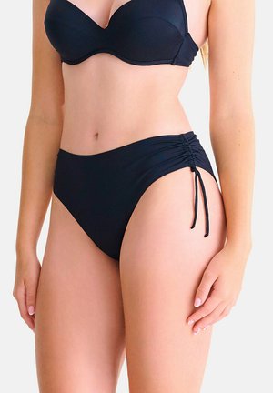 Femme portant un bikini noir avec un haut rembourré et un bas taille haute doté de fronces réglables sur les côtés.
