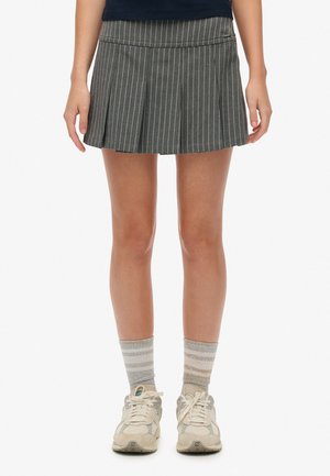 Grijze geplooide rok met witte streepjes, met een platte tailleband. Gepaarde met lichtgrijze gestreepte sokken en beige sneakers.