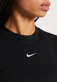 Svart Nike t-shirt med rund halsringning, korta ärmar och vitt Nike-logotyp. Slät tygtextur med en åtsittande design.