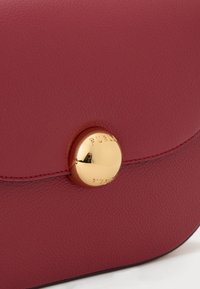 Borsa a mano in pelle bordeaux con un clasp circolare dorato con la scritta "FURLA" incisa, texture liscia e design elegante e minimalista.