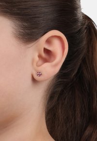 Orecchino a forma di stella rosa con tre pietre scintillanti di diverse tonalità di rosa, montato in metallo argentato, in primo piano su un orecchio.