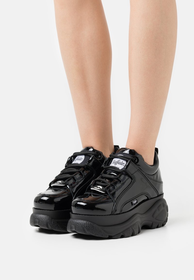 Sorte patenterede lædersneakers med en chunky sål, der har lagdelt design, snørebåndslukning og et logomærke på siden.