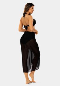 Czarny strój kąpielowy z halterem, ozdobiony kokardką oraz przezroczystą spódniczką o wysokim stanie. Gładka tekstura, minimalistyczny design.