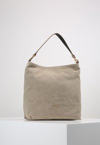 Beige suède handtas met een enkele schouderriem en gouden beslag. Zachte textuur en minimalistisch ontwerp, voorzien van een zichtbaar merknaam.