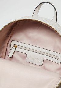 Interno di uno zaino bianco con rivestimento in satin rosa, una tasca con zip e il logo Liu Jo Milano impressa sul pannello della tasca.
