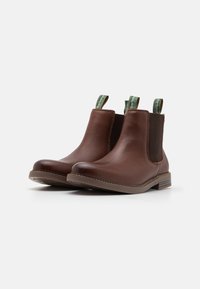 Bottines Chelsea en cuir marron avec des panneaux élastiques sur les côtés, des tirettes vertes, un bout arrondi et des coutures contrastantes sur un petit talon.