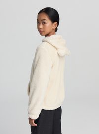 Kremowa kurtka z polaru z kapturem, cechująca się miękką fakturą, długimi rękawami i luźnym krojem. Prosty design bez ozdób.