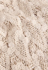 Kohev kreemika värvusega kootud kangas, millel on lillelised roosimustrid, avatud võrgusilmad ning pehme ja tekstuurse olemusega.