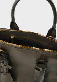 Donkergroene leren handtas met een gouden ritssluiting, voorzien van twee handvaten en een binnenvak met rits. Gladde textuur met minimale metalen details.