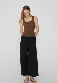 Top de tirantes ajustado marrón con escote cuadrado, combinado con pantalones sueltos de pierna ancha negros. Textura suave, diseño casual, acentos mínimos.