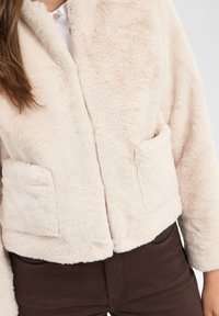 Nepbont jas in lichtbeige met een zachte textuur, voorzien van twee voorzakken, een cropped ontwerp en een brede kraag.