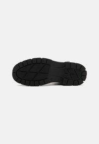 Suela de zapato de goma negra con surcos profundos para tracción, con una superficie texturizada y un talón reforzado para mayor durabilidad.