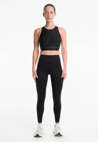 Haut de sport noir court et leggings taille haute, présentant un design épuré, un tissu extensible et des accents latéraux contrastés. Texture ressemblant à du daim.