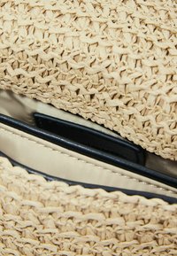 Woven straw bag w kolorze jasnego beżu, z teksturowanym wykończeniem zewnętrznym oraz zipowaną wnętrznością z czarnymi kieszeniami.