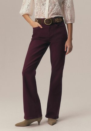 Woman wearing burgundy flare pants, brown belt with round buckle, white floral lace blouse, and taupe pointed-toe kitten heels.