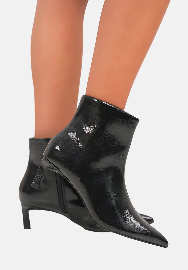 Bottines en cuir verni noir avec un bout pointu et un talon bas et fin. Texture lisse et design épuré avec fermeture éclair.