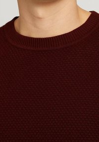 Bordowy sweter dziany z fakturowanym wzorem i prążkowanym, zaokrąglonym dekoltem. Tkanina wydaje się miękka i lekko gruba.