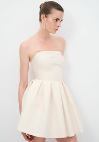 Robe beige sans bretelles avec un corsage ajusté et une jupe évasée. Tissu lisse avec une texture subtile et des détails plissés.