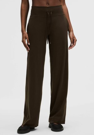 Hnědé kalhoty s úzkým pasem a širokými nohavicemi se stahovacími šňůrkami, které má na sobě osoba stojící na jednoduchém světlém pozadí.