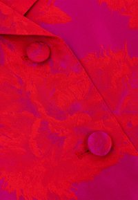 Rode stof met ton sur ton bloemenjacquardpatroon, voorzien van twee beklede knopen en een scherpe kraagrand.